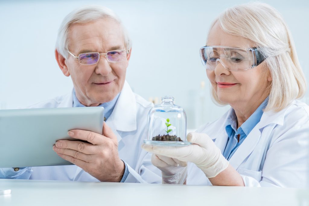 Smiling scientists with digital tablet and green plant in soil